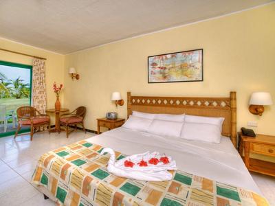 Gemütliches Hotelzimmer mit großem Bett, zwei Sesseln und Blick auf Garten durch offene Terrassentür.