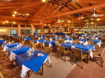 Großes Restaurant mit blauen Tischdecken und vielen gedeckten Tischen unter einer Holzdecke.