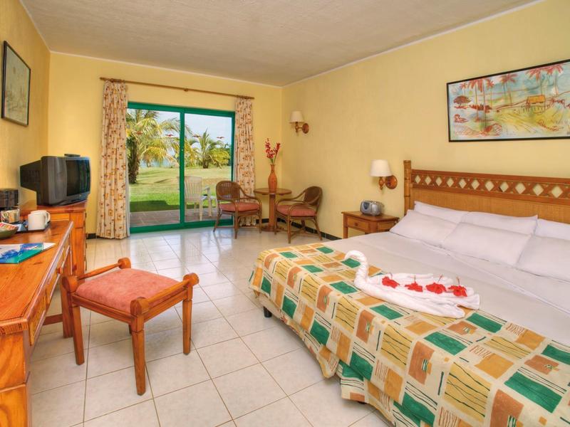 Helles Hotelzimmer mit großem Bett, Schreibtisch, Stuhl und Blick auf Garten durch Schiebetür.