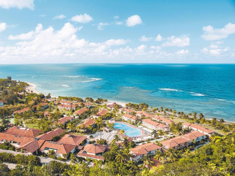 Blick auf ein tropisches Resort mit Pool an der Küste unter blauem Himmel.