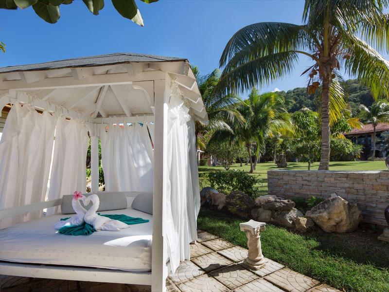 Weißes Himmelbett mit Vorhängen neben Palmen und Garten im Freien.