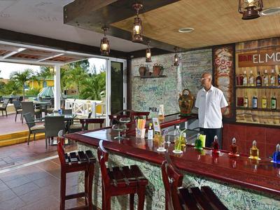 Offene Bar im Hotel mit Holztresen, mehreren Stühlen und Blick auf Palmen und Terrasse.