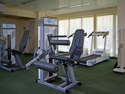 Moderner Fitnessraum mit Trainingsgeräten und Laufband vor großen Fenstern.