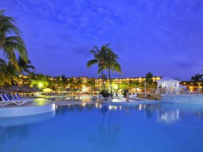 Beleuchteter Poolbereich eines Hotels in der Abenddämmerung mit Palmen und Liegestühlen