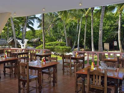 Offener Außenbereich eines Restaurants mit Holztischen und Blick auf tropische Pflanzen.
