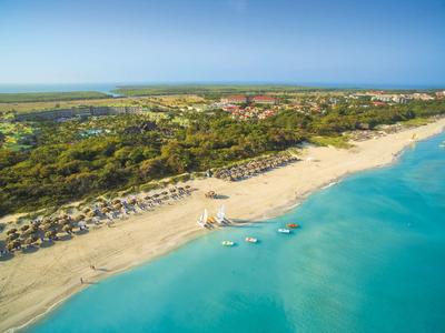 Strand mit türkisblauem Wasser, Sonnenschirmen und grüner Vegetation im Hinterland.