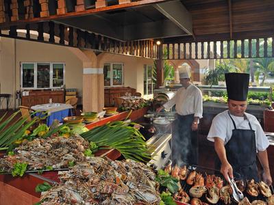 Zwei Köche bereiten in einer offenen Küche frische Meeresfrüchte mit Holzdekoration und Pflanzen vor.