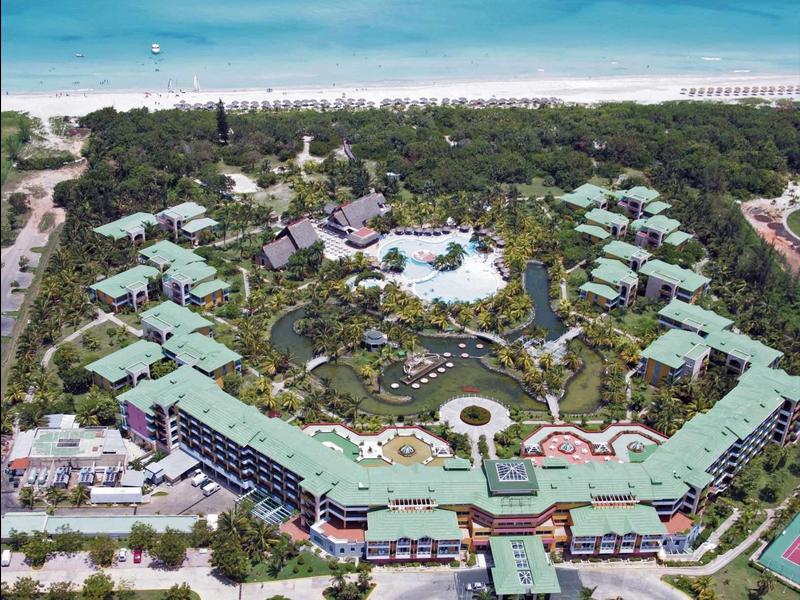 Noční osvětlený hotelový bazén s palmami a lehátky.