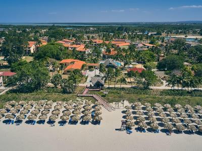 Veduta aerea di una spiaggia con ombrelloni, lettini e un complesso alberghiero sullo sfondo.