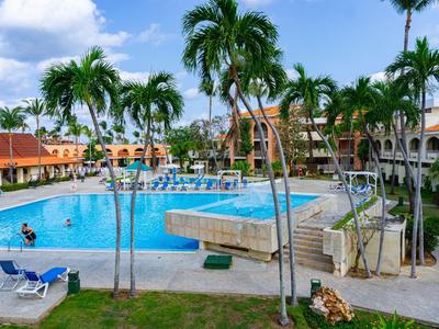 Piscina dell'hotel con sdraio e palme sotto un cielo azzurro in un ambiente tropicale.