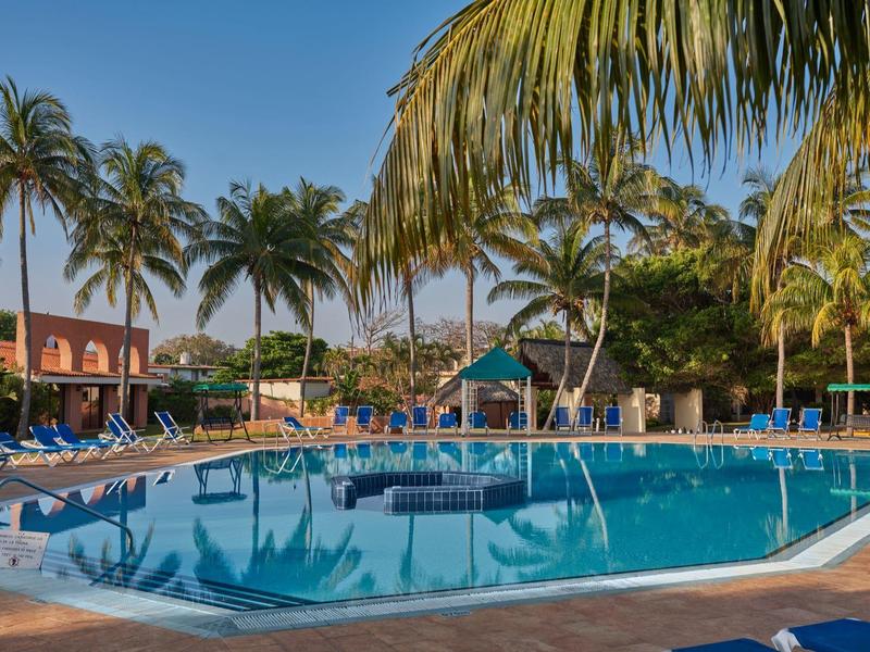 Area piscina limpida con lettini e palme in un hotel tropicale al tramonto.