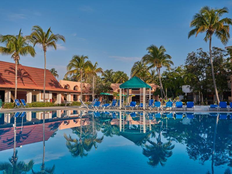 Grande piscina dell'hotel con area giochi acquatica e palme sotto un cielo limpido.