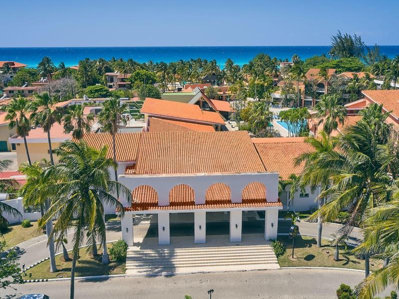 Complesso alberghiero con tetti rossi e palme vicino a un mare blu in una giornata di sole