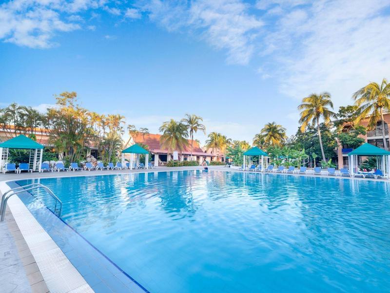 Grande piscina all'aperto con lettini e palme in un resort alberghiero sotto un cielo limpido.