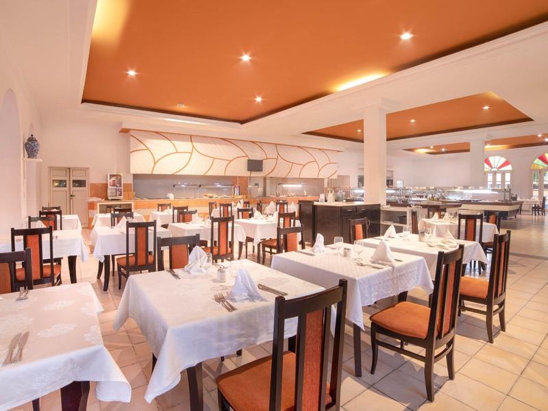 Ristorante luminoso e moderno con tavoli apparecchiati e accenti arancioni caldi sul soffitto.
