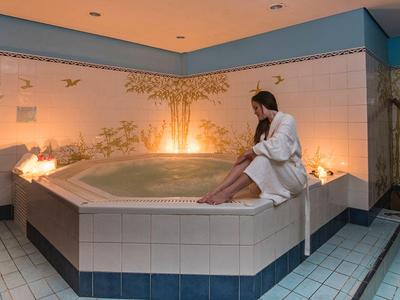 Person in a bathrobe sits on the edge of a lit jacuzzi in a stylish spa area.