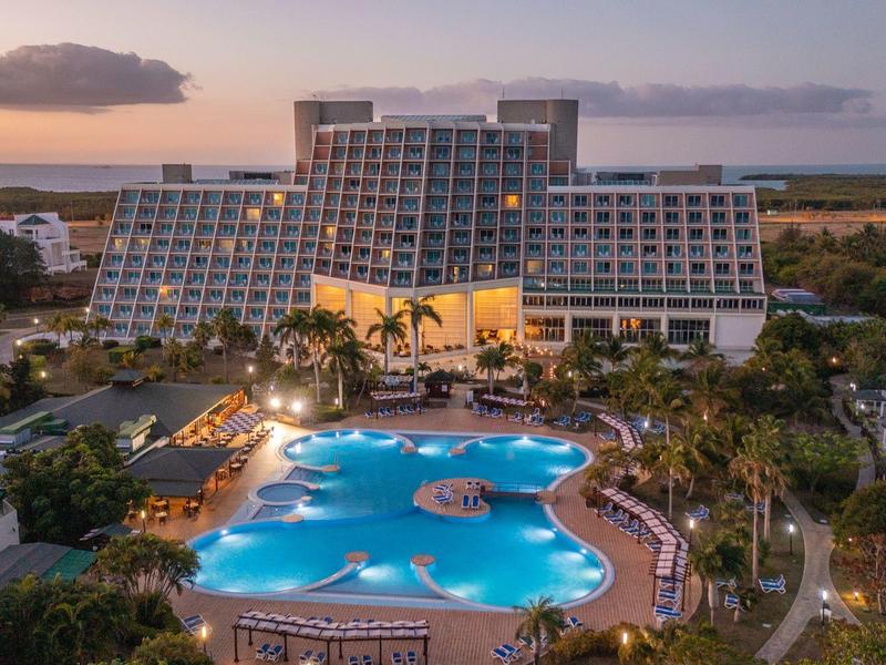 Hotel di lusso con grandi piscine e palme al tramonto vicino alla costa.
