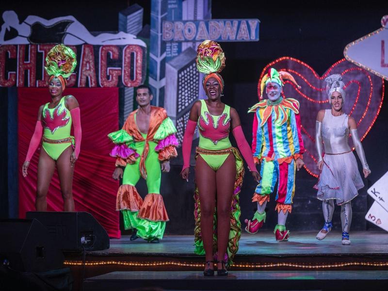 Spettacolo colorato con cinque artisti sul palco in costumi vivaci e oggetti di scena luminosi.