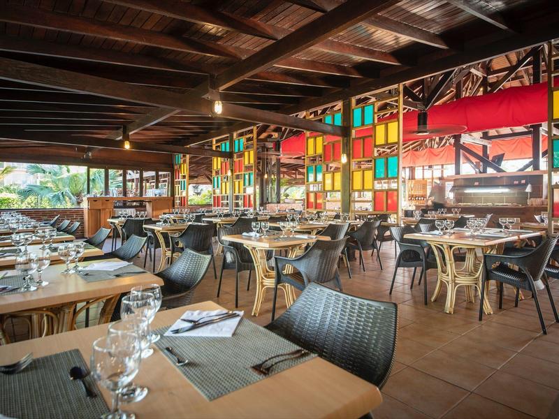Interno di un ristorante con soffitto a travi di legno, finestre colorate e tavoli apparecchiati.