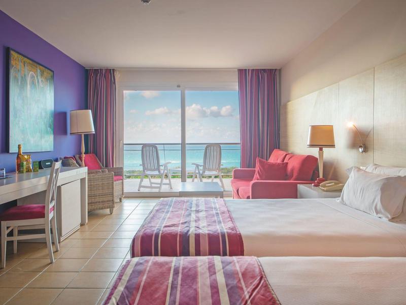 Camera d'hotel moderna con due letti, balcone e vista mare alla luce del giorno.