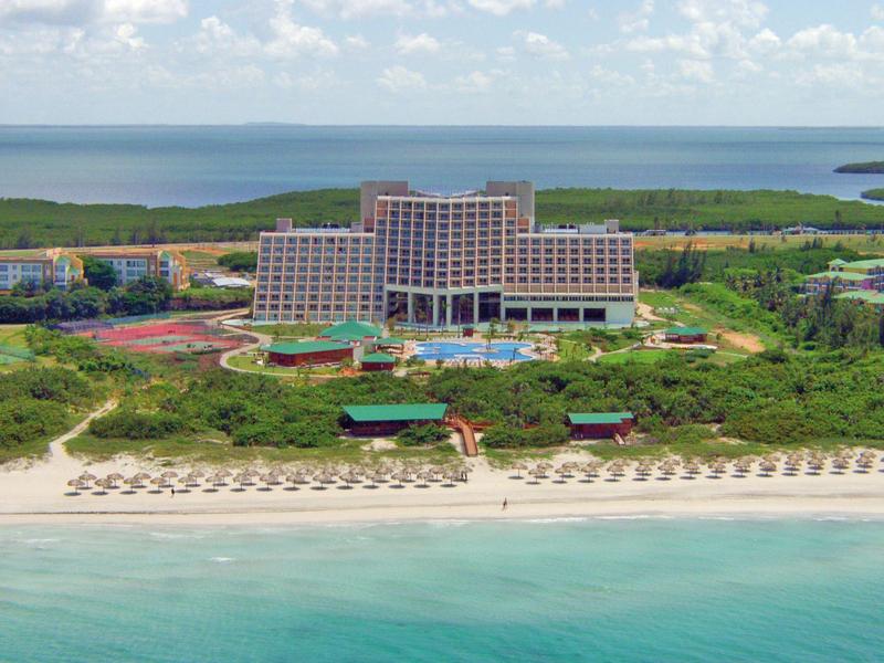 Grande hotel su una spiaggia sabbiosa con lettini e mare turchese.
