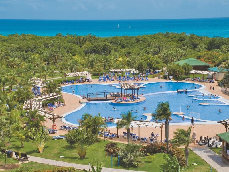 Grande piscina dell'hotel con design circolare e lettini, circondata da una rigogliosa vegetazione tropicale.