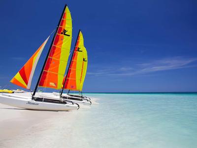 Two colorful sailboats on a clear, shallow beach under a blue sky.
