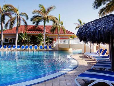 Swimming pool with lounge chairs and palm trees at a sunny vacation spot.