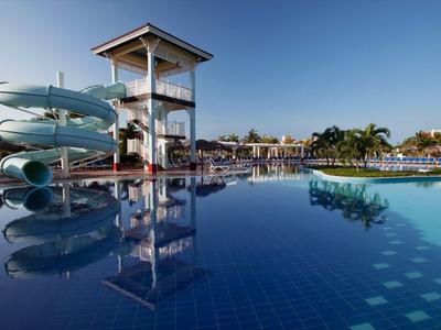 Large pool with water slide and sun terrace under clear sky.
