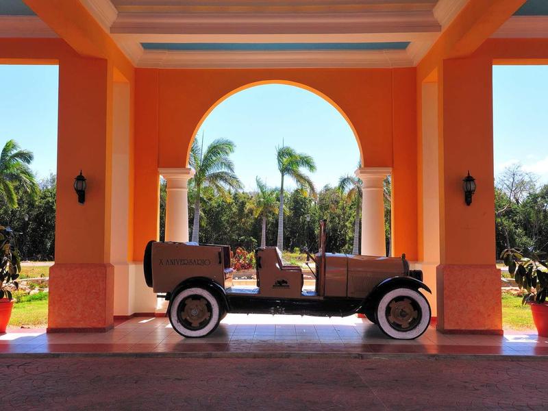 Vintage car under an orange archway with palm trees and blue sky in the background.
