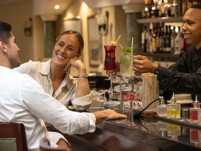 Drei Menschen lachen und stoßen mit Getränken an einer gemütlichen Bar zusammen.