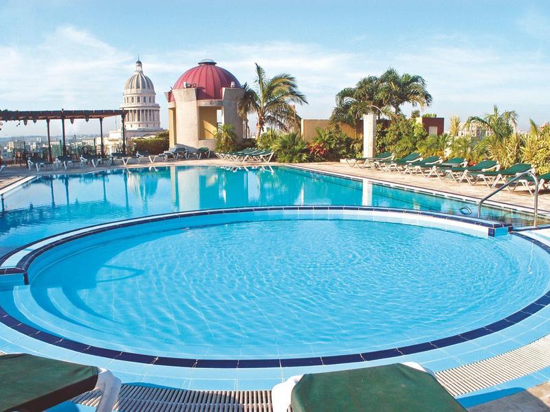 Groot rond hotelzwembad met helder water en parasols onder zonnige lucht.