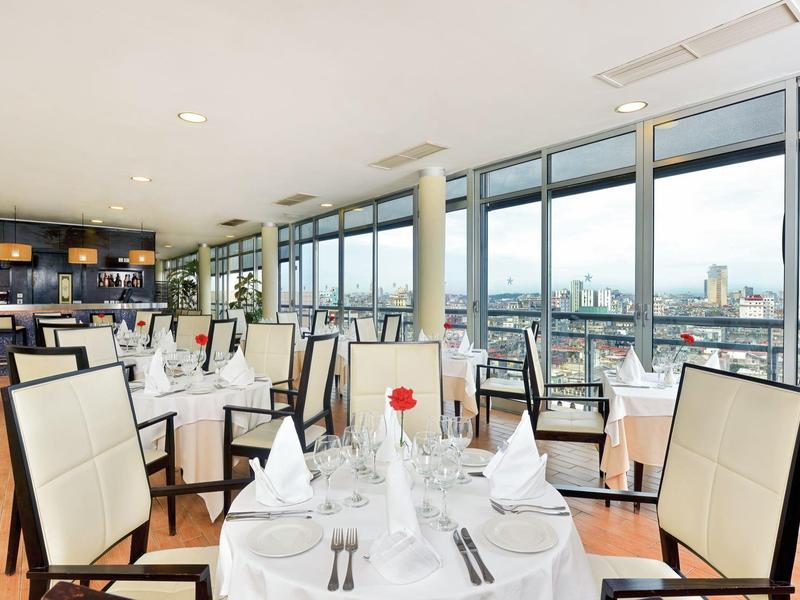 Elegant restaurant met witte tafelkleden en groot panoramisch raam met uitzicht op de stad.