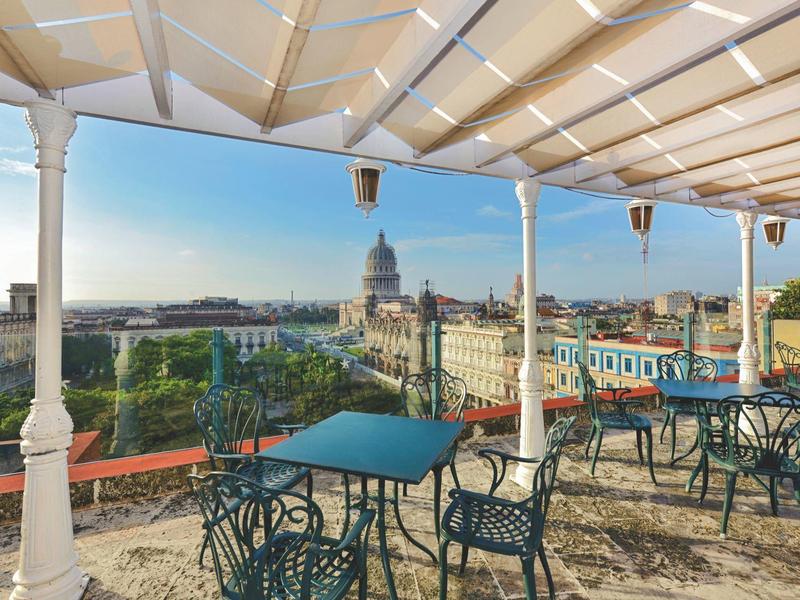 Dakterras met tafels en stoelen met uitzicht op stad en markante gebouwen.