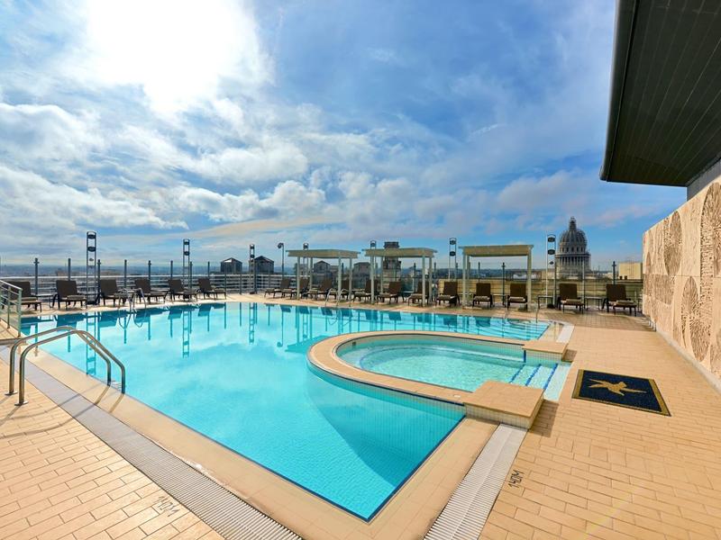 Groot verwarmd buitenzwembad met trappen en terras, bewolkte lucht op de achtergrond.