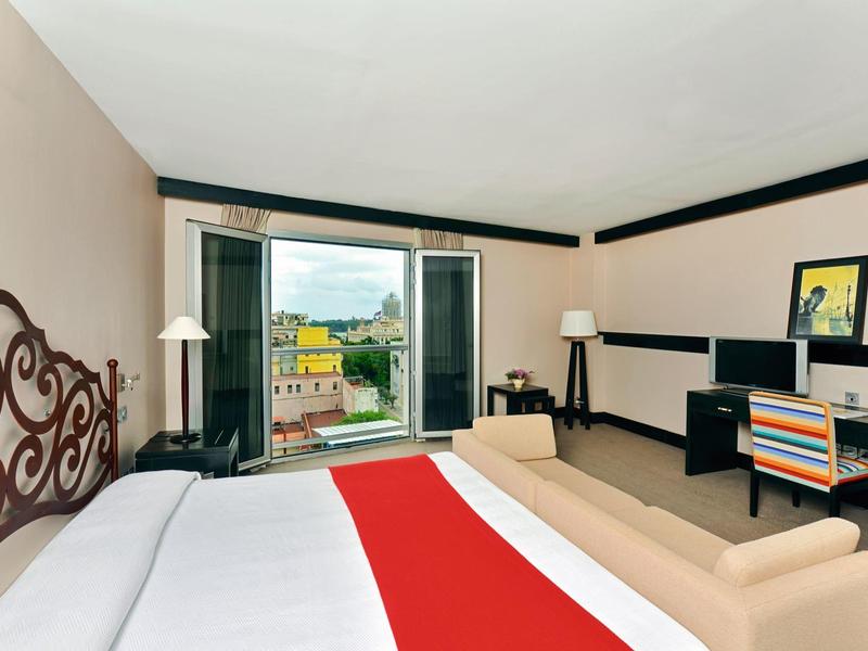 Hotelkamer met groot bed, rode loper, bank, bureau met stoel en balkon met uitzicht.