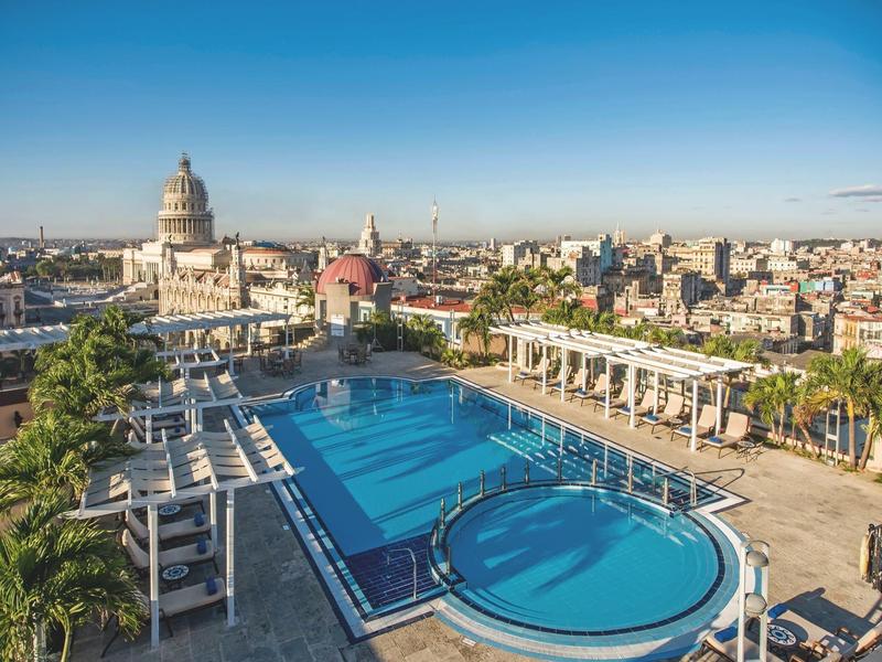 Dakterras met groot zwembad en uitzicht op historische stadsgezichten bij heldere hemel.