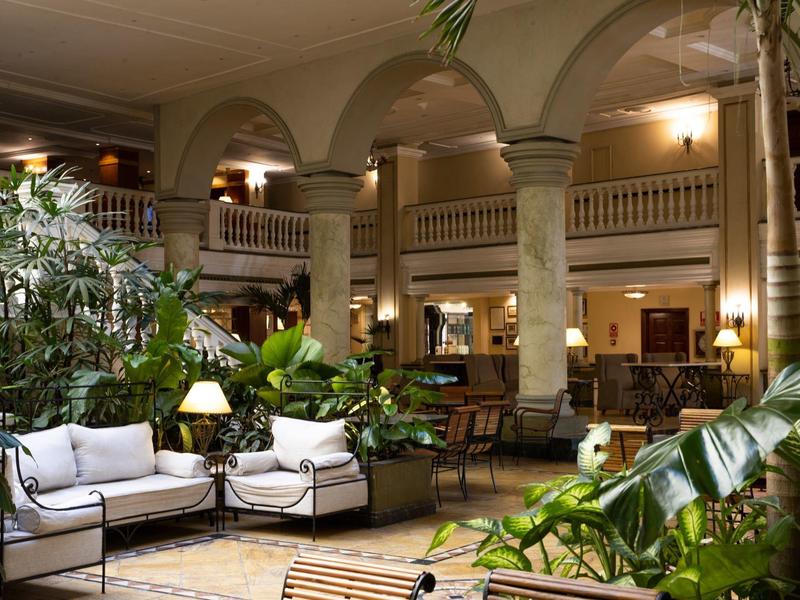 Elegante hotellobby met hoge zuilen, groene planten en gezellige zithoeken.