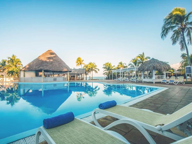 Area piscina con lettini e palme in una struttura alberghiera soleggiata.