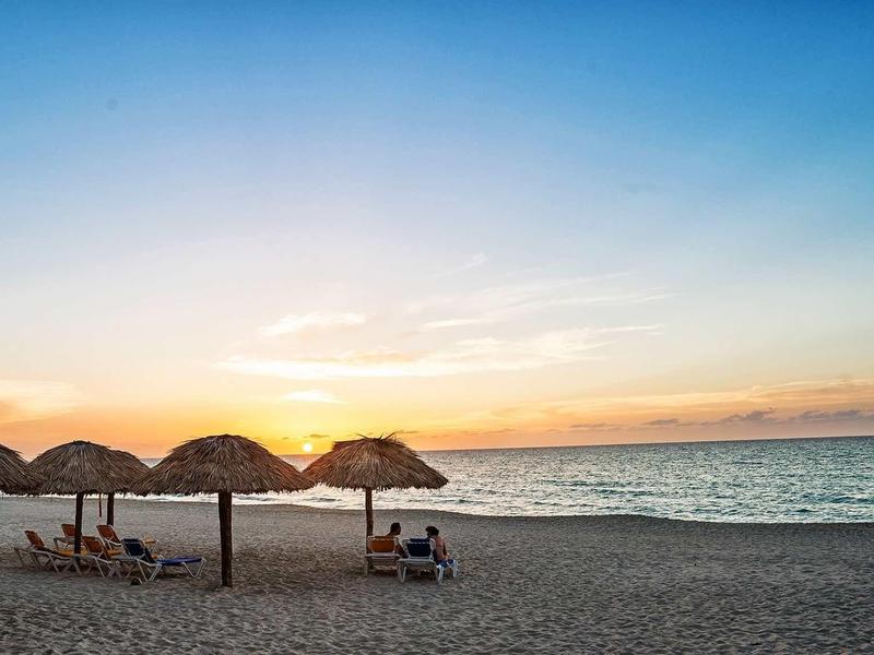 Strand mit Sand, Sonnenschirmen aus Palmblättern und Sonnenuntergang am ruhigen Meer.