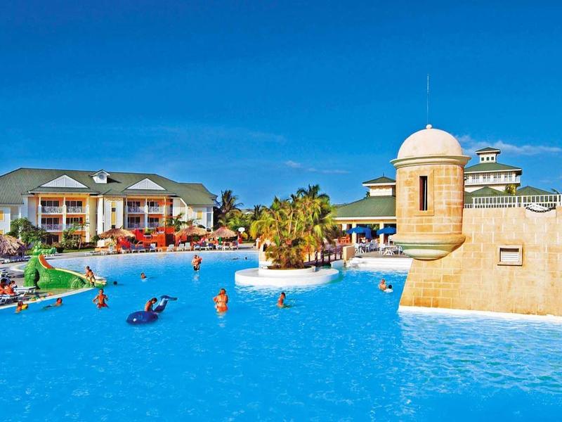 Grande struttura alberghiera con piscina esterna blu e cielo limpido.