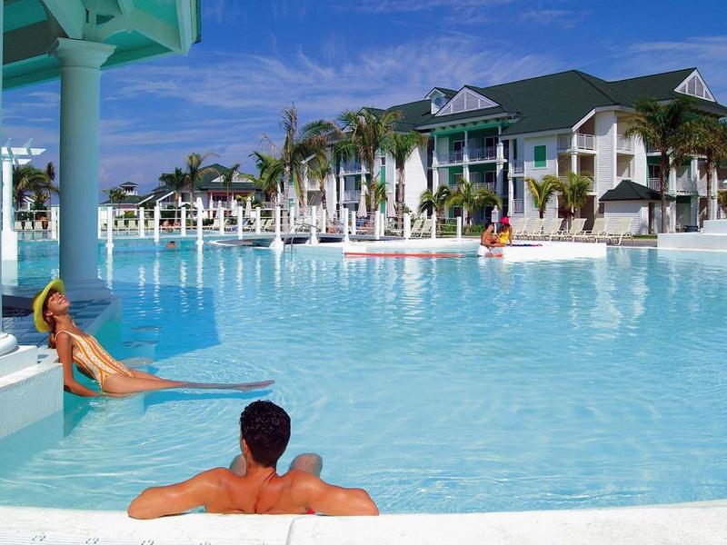 Coppia a bordo di una grande piscina davanti a un hotel sotto un cielo azzurro.