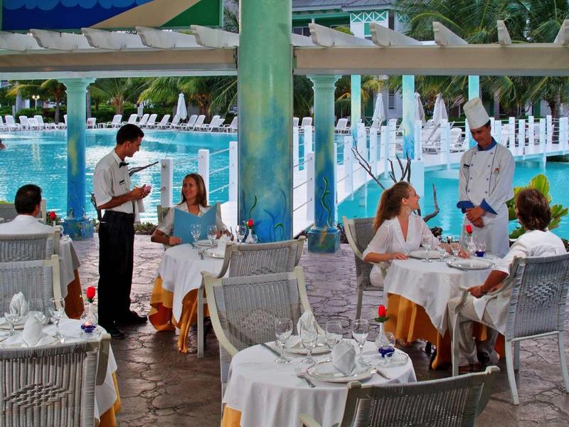 Terrazza di ristorante sul mare con tavoli bianchi e camerieri al lavoro.