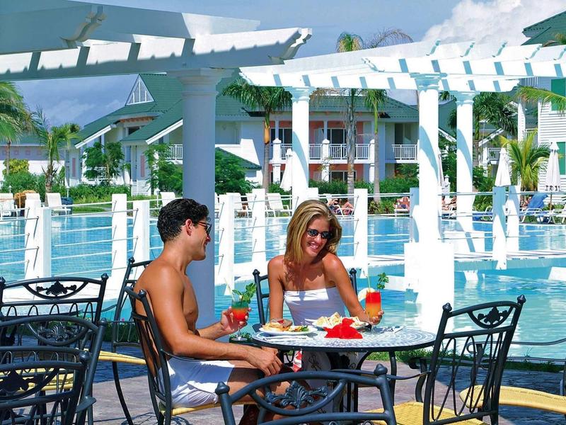 Due persone mangiano e bevono vicino a una piscina in un ambiente di vacanza soleggiato.