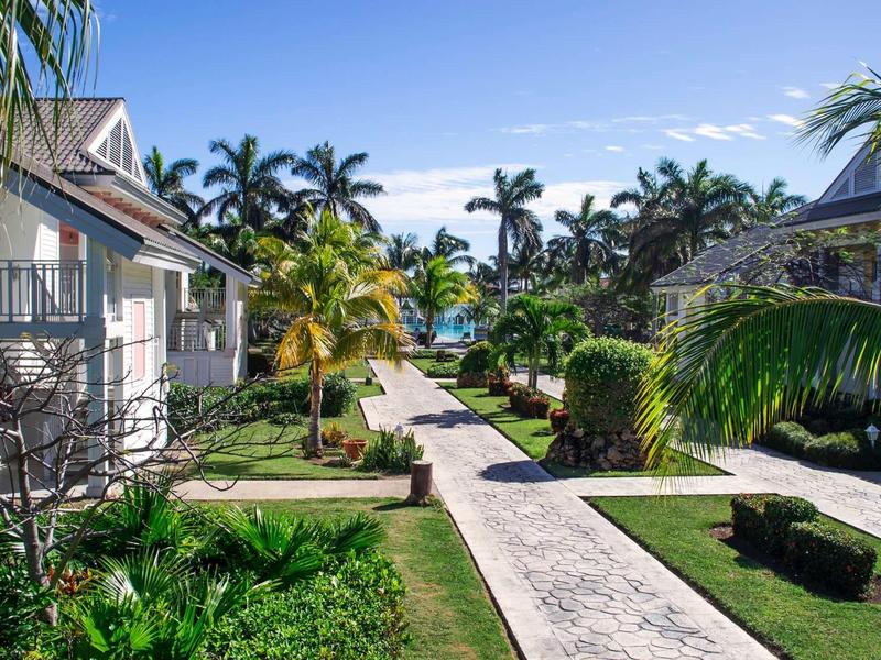 Sentiero lastricato tra bungalow circondati da palme sotto un cielo azzurro.