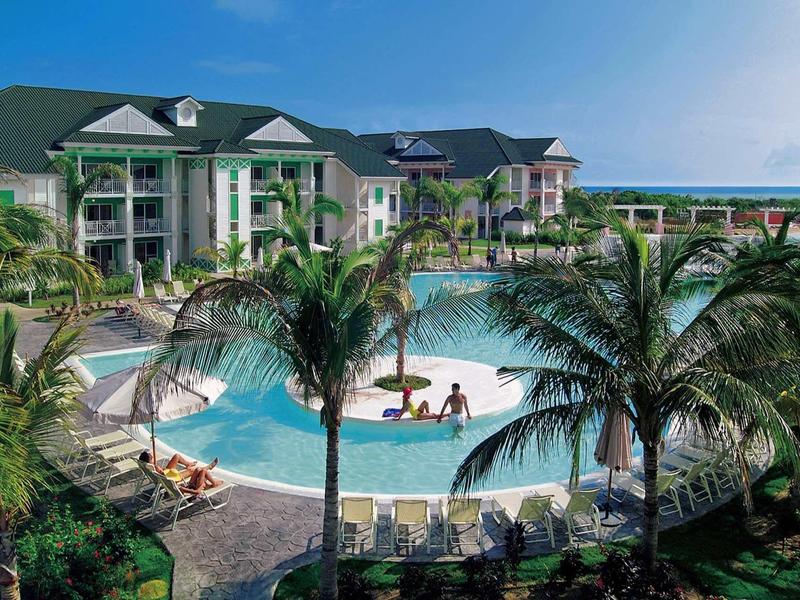 Piscina rotonda in un hotel con palme e sdraio, sotto un cielo azzurro.