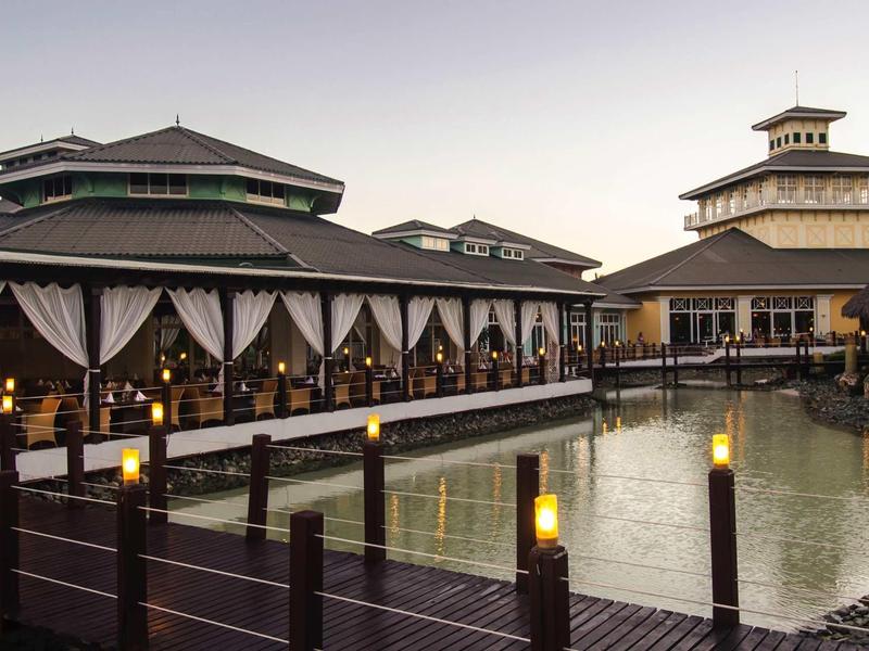 Hotel sull'acqua con passerelle in legno e luci calde al tramonto.