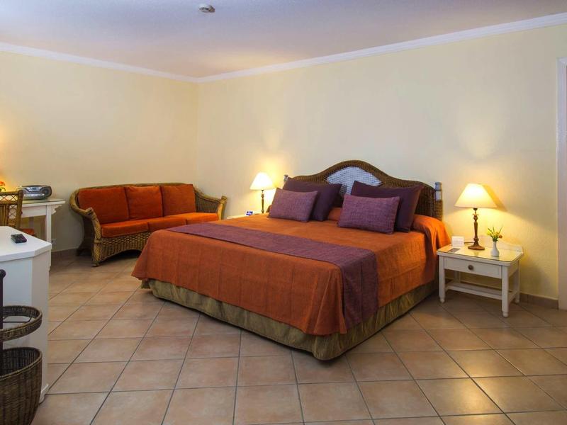 Camera d'albergo con letto grande, divano arancione e lampade su comodini bianchi.