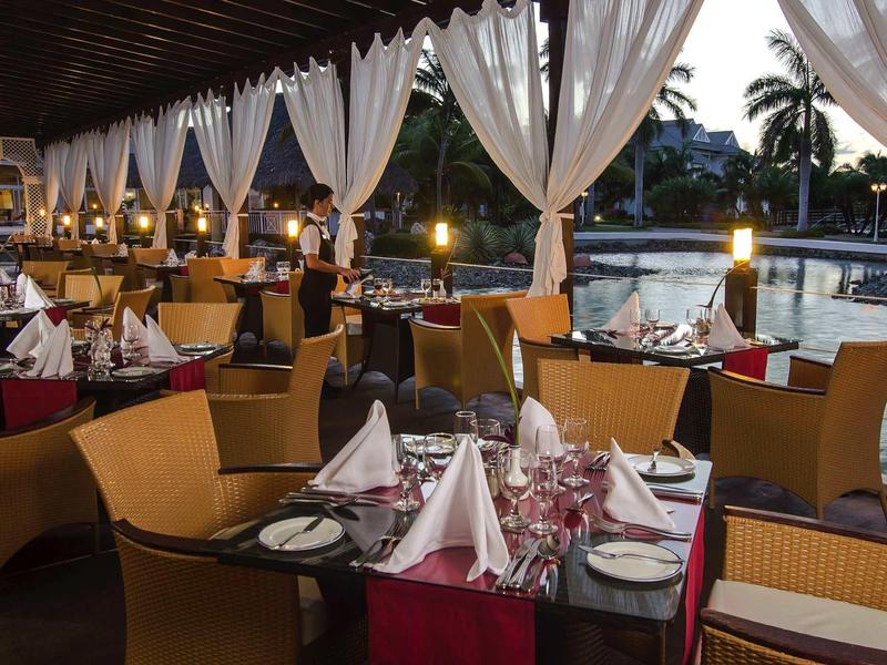 Terrazza di ristorante elegante con tavoli apparecchiati vicino all'acqua e luci soffuse.