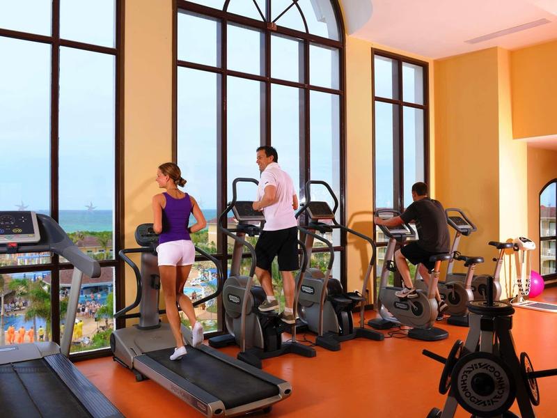 Tre persone si allenano in una palestra con grandi finestre che si affacciano sulla città.